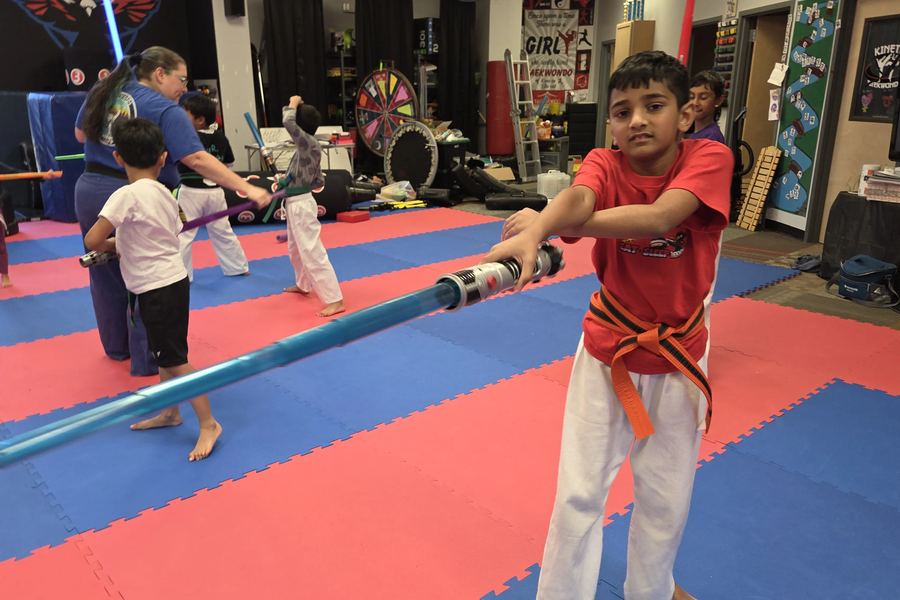 A young Kinetic student in an orange belt during a lightsaber class
